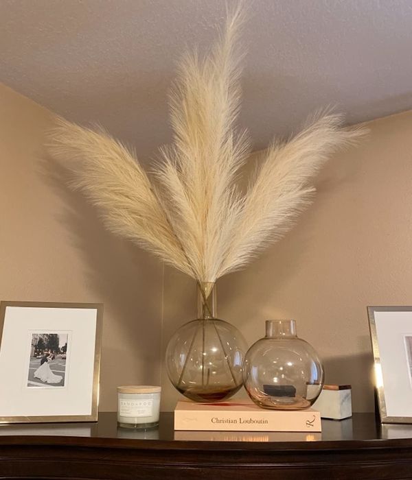 Reviewer photo of beige faux pampas plumes in a glass vase, resting atop a wooden cabinet.