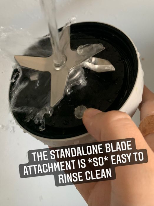 My hand holding the blade attachment under the faucet to rinse it clean