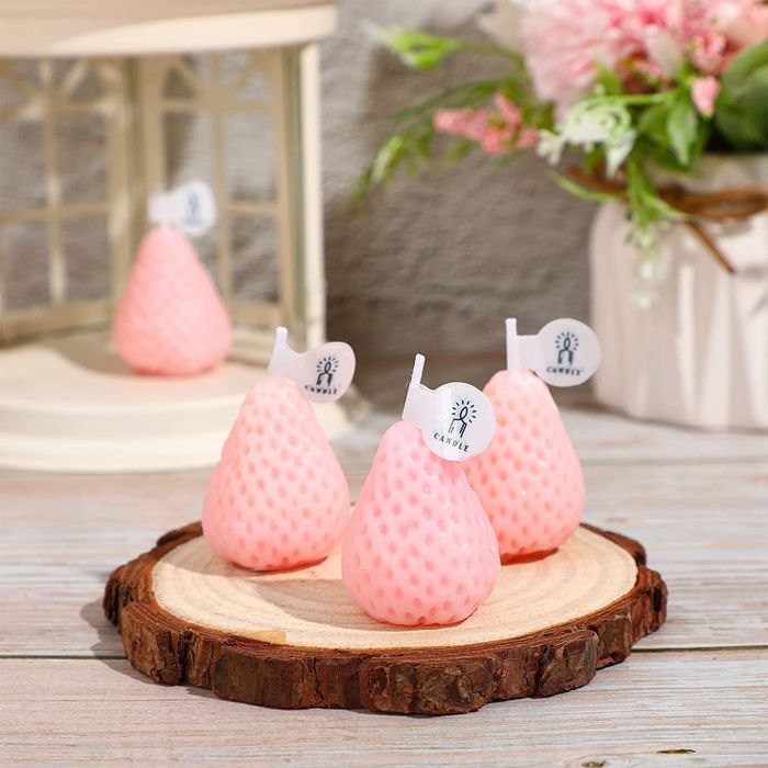 A set of four soft pink strawberry-shaped candles placed on a table.
