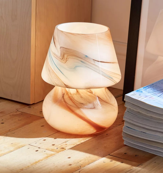 The vibrant, multicolored lamp placed on a wooden floor next to a stack of magazines.