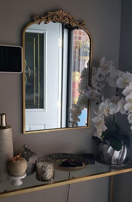 The mirror placed over a gold and glass foyer table.