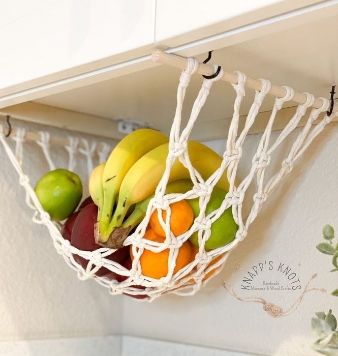 A white macrame fruit hammock attached to the bottom of a cabinet, neatly storing fresh produce.