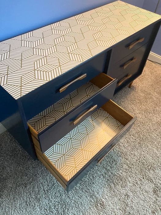 A reviewer’s black chest of drawers, with the top and the interior of each drawer covered in elegant white and gold geometric wallpaper, bringing a touch of luxury and style.