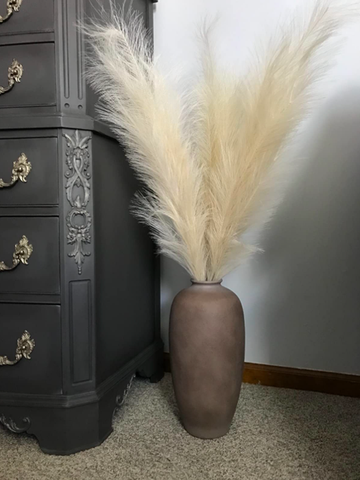 Tan pampas grass in a vase placed beside a black dresser
