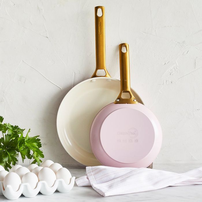 The two pink pans propped up against the wall on a kitchen counter, accompanied by a towel, eggs, and fresh herbs