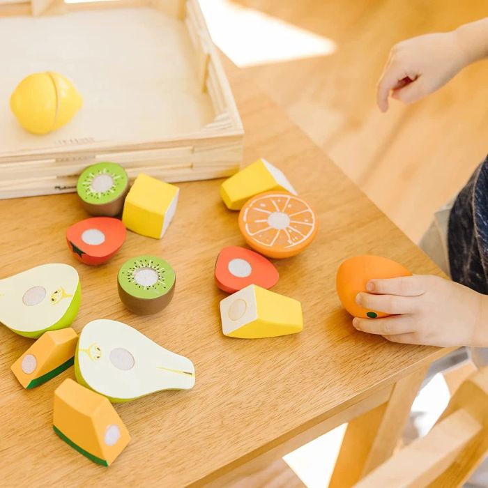 a collection of wooden fruit displayed on a table, featuring kiwi, pears, oranges, bananas, cantaloupe, strawberries, and a lemon