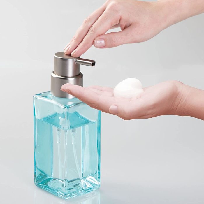 A person using a light blue foaming soap dispenser with clear blue soap to dispense foam onto their hand.