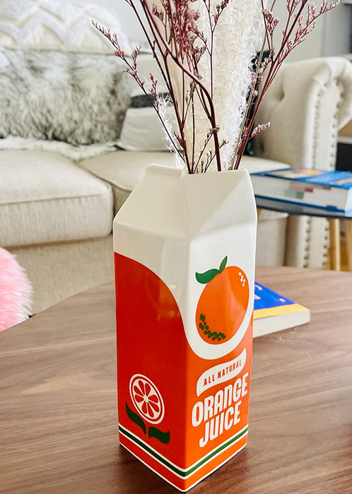 A photo from a reviewer showcasing the orange juice carton vase placed on a table, adding vibrant charm to the space.