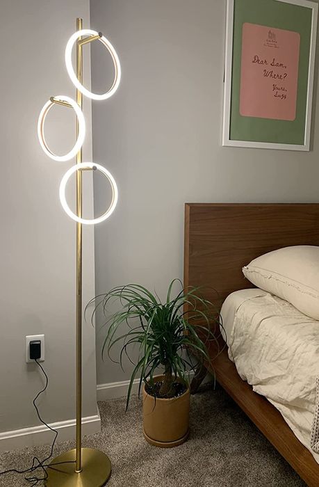 A tall, gold-colored floor lamp featuring three rings, each one illuminated.