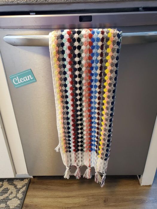 A vibrantly patterned crocheted towel drapes over the handle of a dishwasher, adding a touch of color to the kitchen.