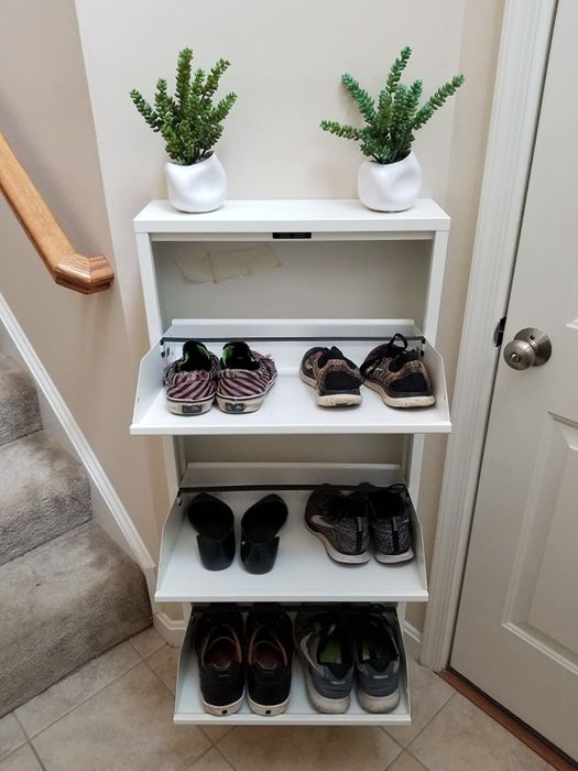 A white, narrow cabinet with three doors folded down to reveal shelves where shoes are neatly stored.