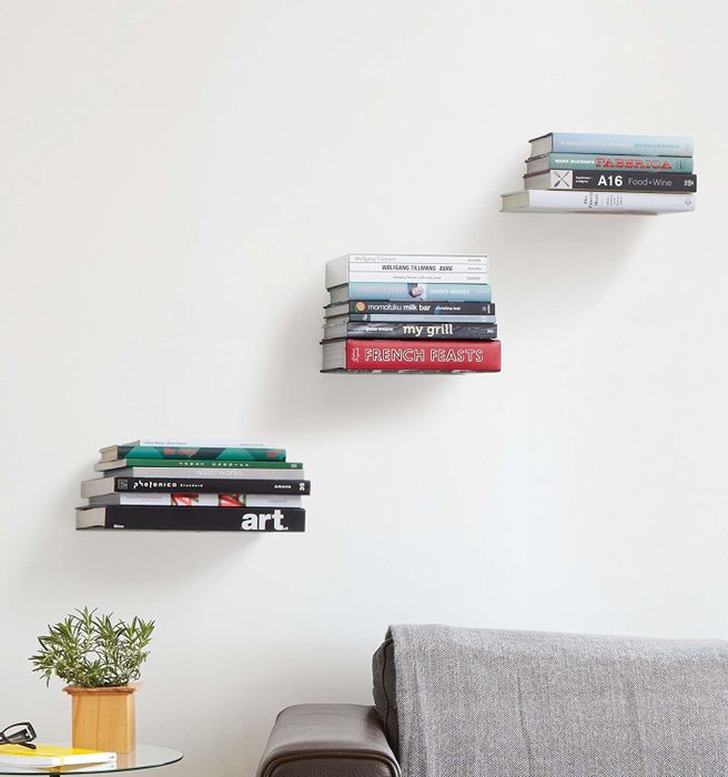 Three stacks of books appear to levitate on shelves mounted on the wall, positioned above a couch.