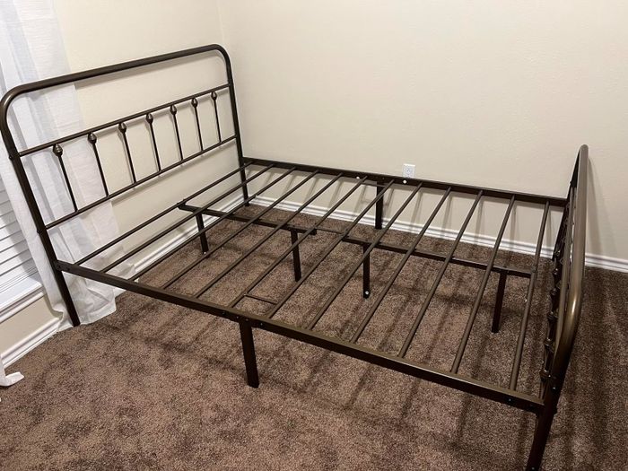 A disassembled metal bed frame with a headboard and footboard, placed in a room without a mattress.