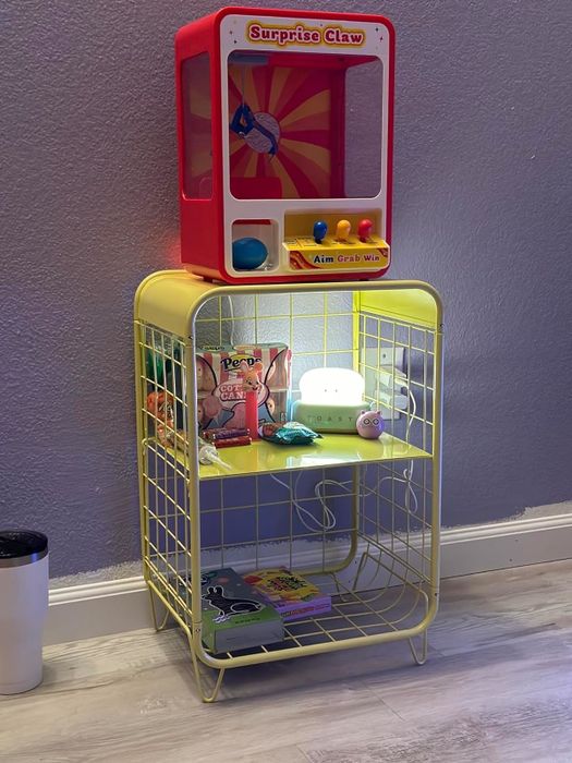 A mini claw machine sitting on a shelf, surrounded by a variety of small items, perfect for a playful room decor.