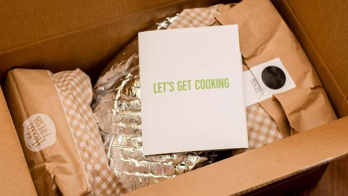 An opened Hello Fresh meal kit displaying various ingredients wrapped in paper and foil packaging.