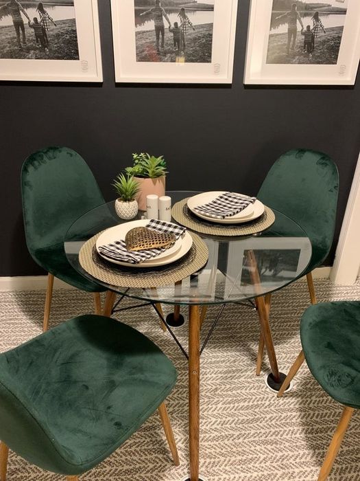 A reviewer's photo of a glass-top table with four sturdy wooden legs.