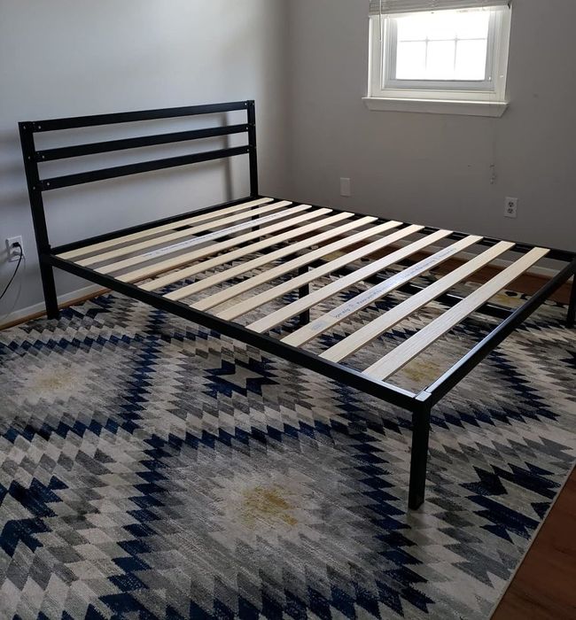A metal bed frame with wooden slats, placed on a geometric patterned rug in a stylish room.