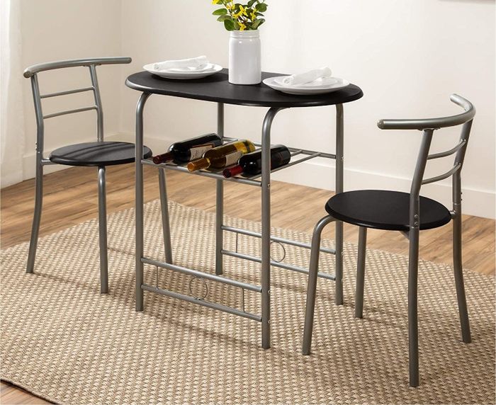 A small, oval-shaped table with a built-in wine rack underneath, accompanied by two compact chairs.