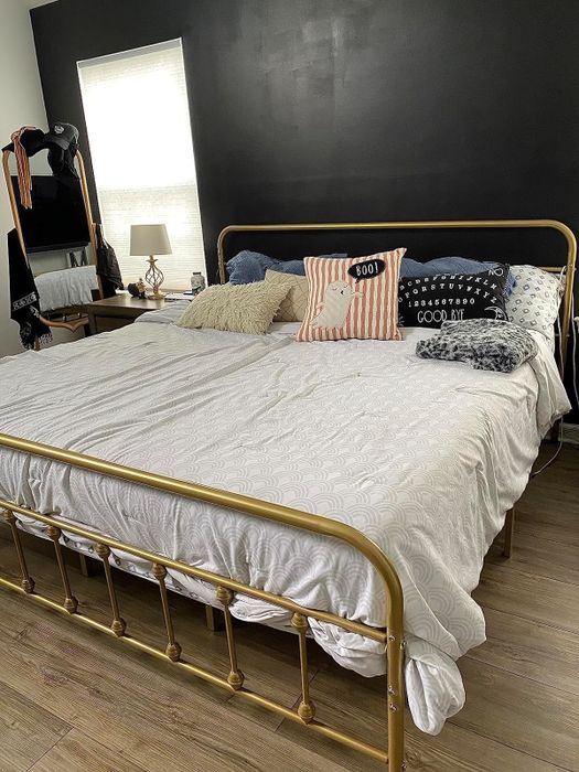 A neatly arranged bed featuring a mix of solid and patterned pillows, paired with a gold-colored bed frame.