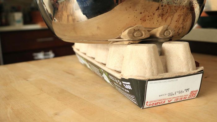 A heavy pot rests on top of an upturned egg carton.