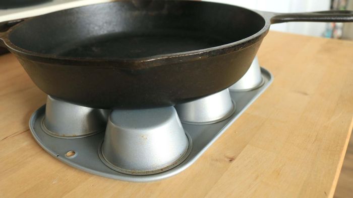 A cast iron skillet rests on an inverted muffin tin.