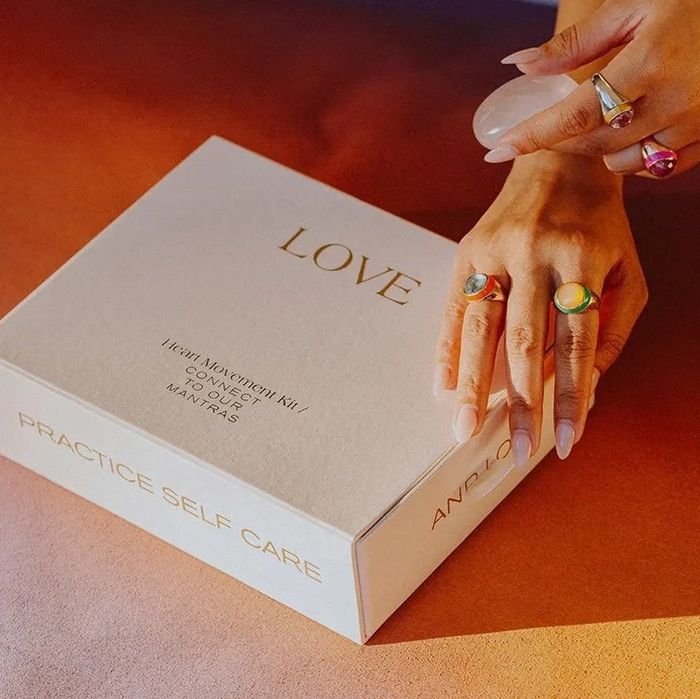 A box containing products with a hand adorned in multiple rings resting on top.