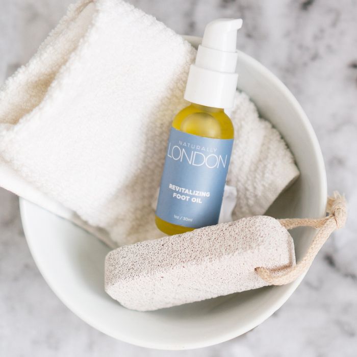 A bowl of oil accompanied by a towel and exfoliating stone.