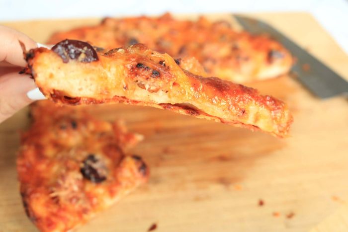 A side view of the pizza slice reveals the visible frico cheese layer.