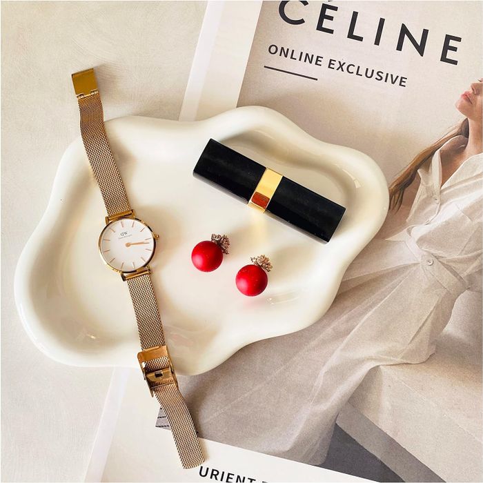 A cloud-shaped dish holding a set of earrings, a watch, and some lipstick.