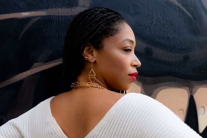 The model is seen from behind, her face turned to reveal several elegant earrings and a chic gold chain necklace.