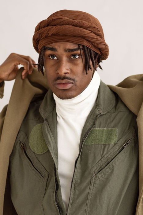 A person styling a wrap by covering the entire top of their head and looping the extra fabric on the edges.