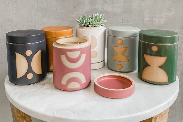 A collection of ceramic candles featuring abstract patterns, lids, and small plants inside.
