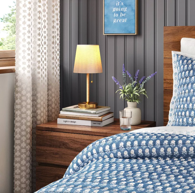 A brass and rattan lamp sitting on top of a stack of books on a nightstand.