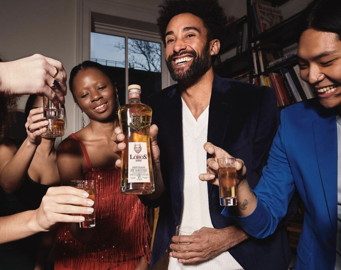 A group of people happily holding up tequila glasses, sharing smiles.