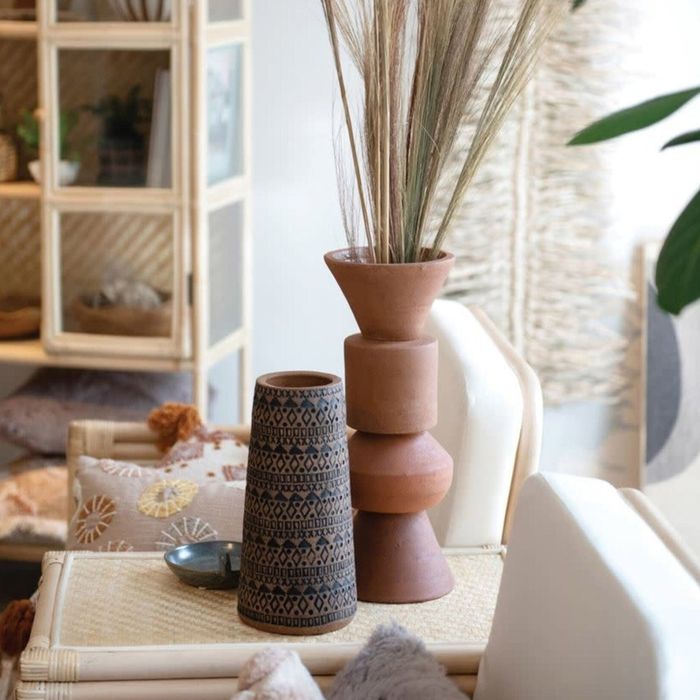 A decorative clay vase with a geometric pattern placed on a table alongside other vases.