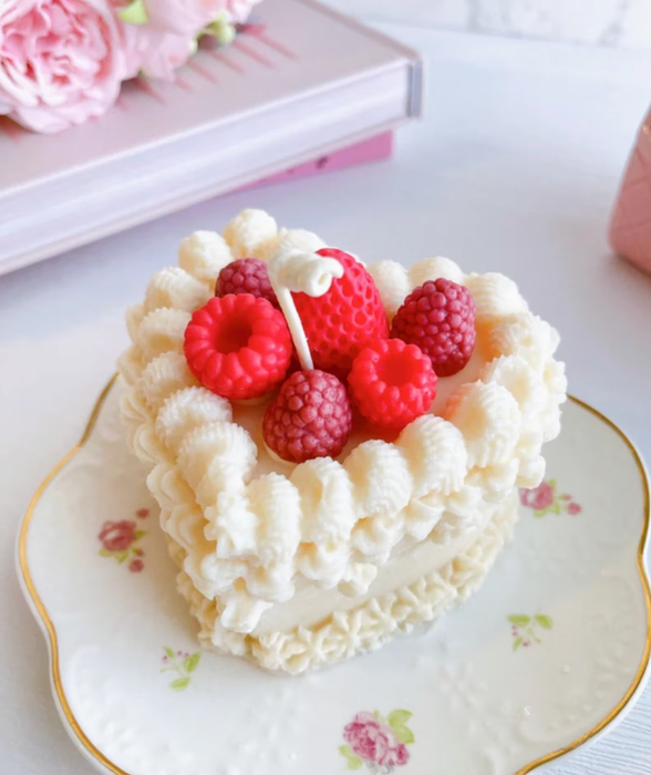 A white cake candle adorned with faux strawberries and raspberries