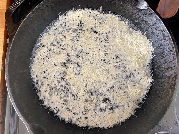 A cast iron skillet with an even layer of shredded parmesan cheese sprinkled on the bottom.