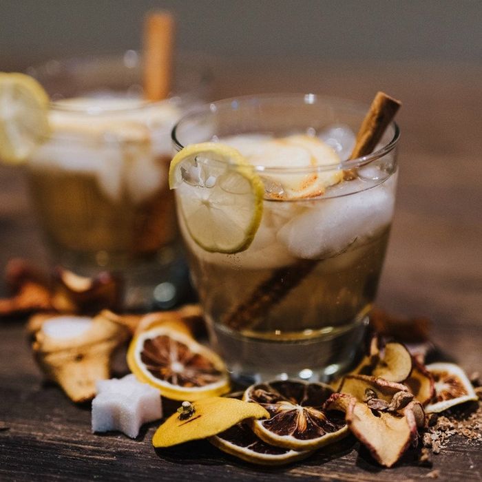 Two apple pie cocktails, each served in a glass with a lime slice and a cinnamon stick.
