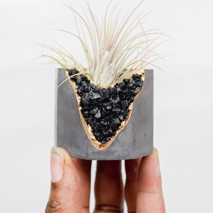 A ceramic mini airplant pot with a broken geode side, beautifully gilded at the edges, and topped with a plant.