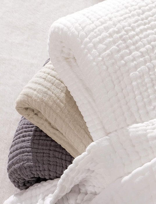 A pile of tan, white, and grey throws stacked together.