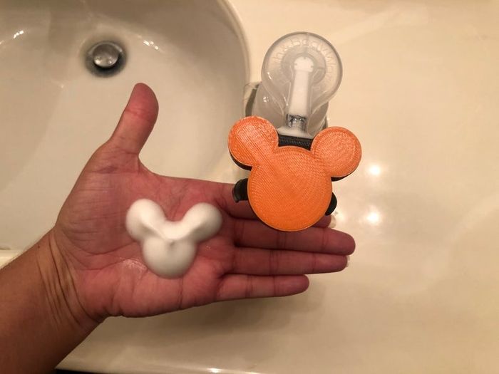 A hand using the orange pump to dispense Mickey face and ears-shaped foam soap