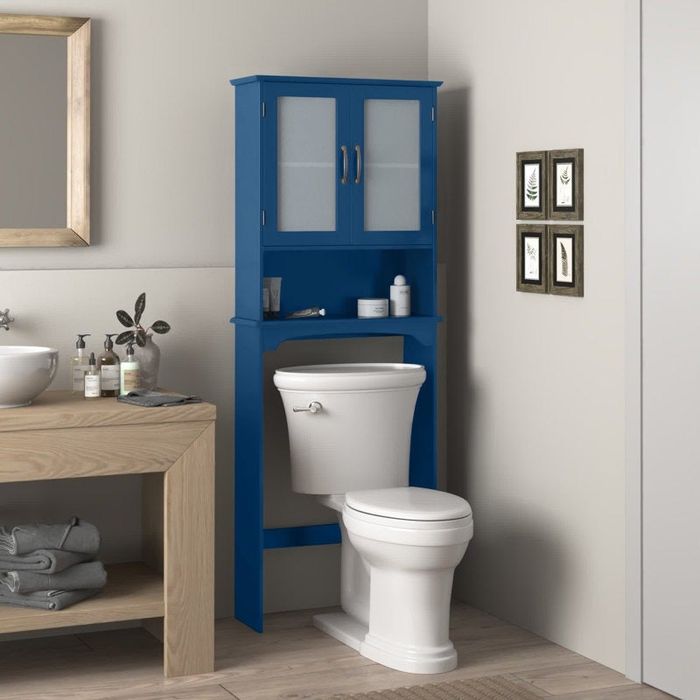 A bathroom featuring a blue over-the-toilet cabinet, a toilet, and minimalist decor, with accents of plants and towels
