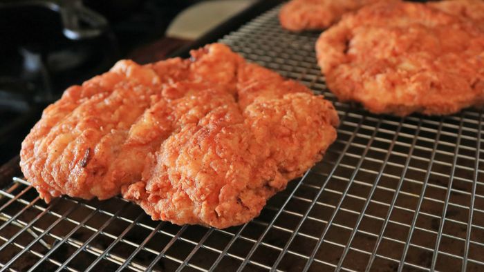Two golden fried chicken cutlets resting on a wire rack.