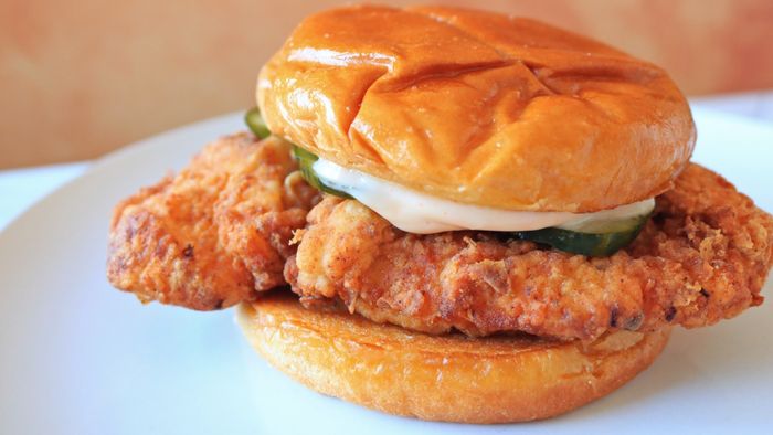 A homemade version of the Popeyes fried chicken sandwich, complete with pickles, served on a white plate.