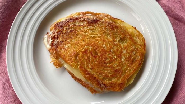 A perfectly crispy grilled cheese sandwich made with croissant bread, plated on a white dish.