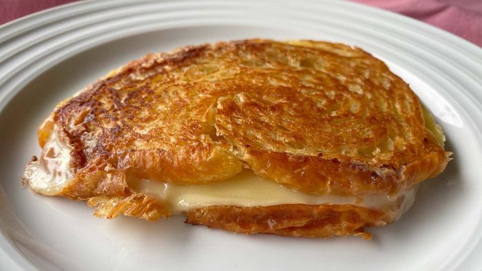 A close-up of the beautifully finished sandwich, golden and crispy with melted white cheese spilling from the edges.