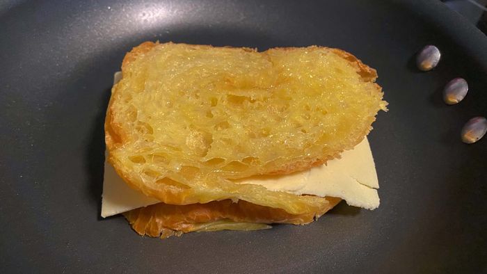 The grilled cheese croissant sandwich sizzling away in the pan.
