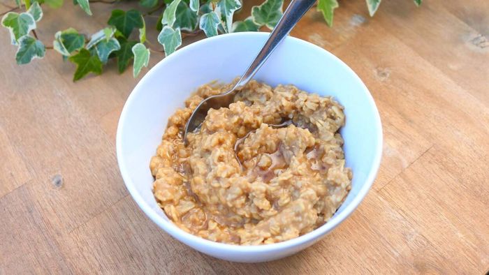 A steaming bowl of oatmeal with a drizzle of honey sits on a table, with ivy gently climbing in the background.
