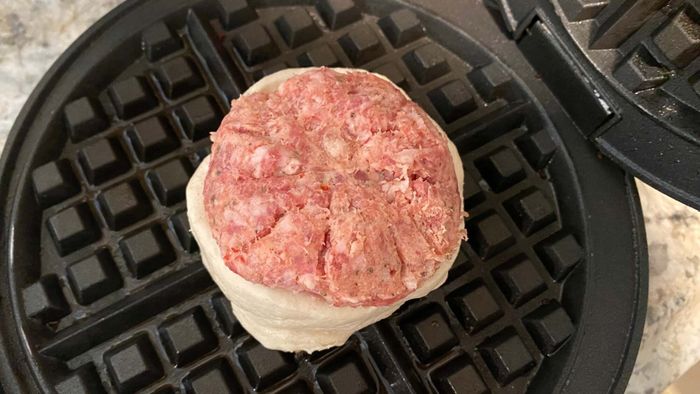Raw biscuit dough and sausage patty placed inside a preheated waffle iron