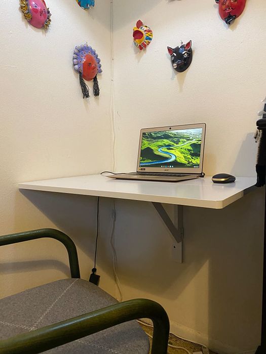 A white wall-mounted desk, fully extended, with a laptop placed on top of it, as seen in the reviewer's setup.